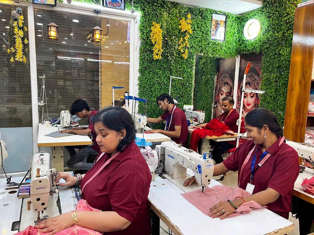 Four tailors at their machines, working on pink and red cloth.
